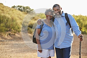 Portrait Of Senior Couple Wearing Backpacks Hiking In Countryside Together