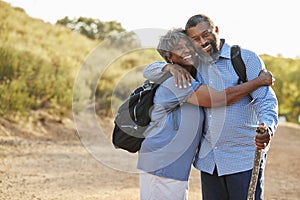 Portrait Of Senior Couple Wearing Backpacks Hiking In Countryside Together