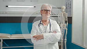 Portrait of senior doctor standing with arms crossed in cabinet