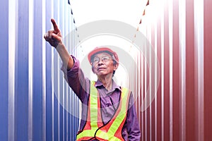 Portrait of senior elderly Asian worker engineer wearing safety vest and helmet, pointing to camera, standing between red and blue