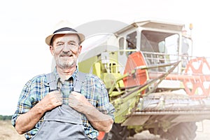 Portrait of Senior farmer standing against combine harvester at farm