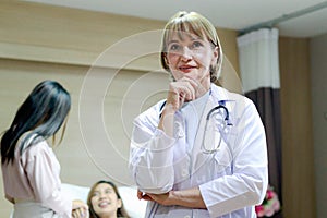 Portrait of senior female doctor in workwear with stethoscope standing and thinking and taking decisions with hand on chin in