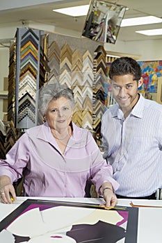 Portrait of senior female owner with customer measuring picture frame