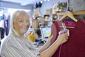 Portrait Of Senior Female Volunteer Working In Charity Shop Or Thrift Store Selling Used And Sustainable Clothing