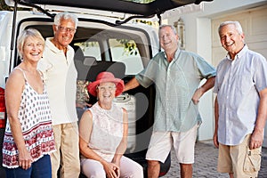 Portrait Of Senior Friends Loading Luggage Into Trunk Of Car About To Leave For Vacation