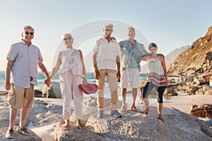 Portrait Of Senior Friends Standing On Rocks By Sea On Summer Group Vacation