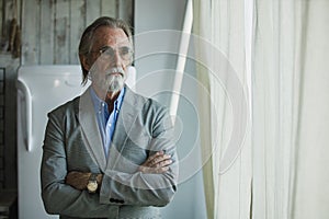 Portrait of senior handsome man wear eyeglasses with grey hair and beard arms crossed look out window. businessman grandfather