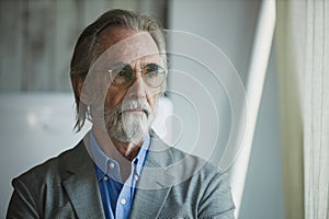 Portrait of senior handsome man wear eyeglasses with grey hair and beard arms crossed look out window. businessman grandfather