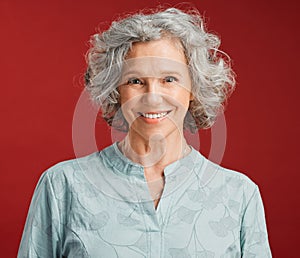 . Portrait of senior, happy and cheerful woman standing against a red studio background. Mature woman with healthy