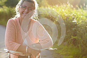 Portrait, senior and happy woman on bicycle in nature for exercise, wellness and health outdoor. Face, smile and elderly
