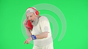 Portrait of senior hipster on Chroma key green screen, cool old man in headphones with speaker jamming to music