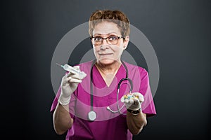 Portrait of senior lady doctor holding syringe and pills