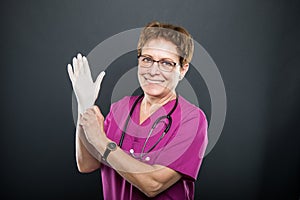 Portrait of senior lady doctor putting on sterile gloves