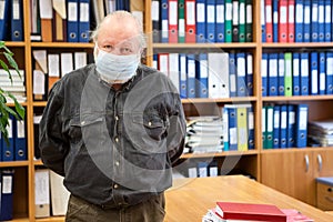 Portrait of senior male archivist with hands behind back looking at camera, man wearing facial mask due coronavirus pandemic,