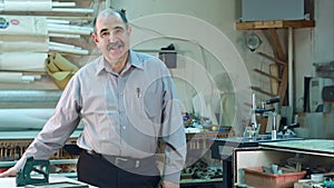 Portrait of a senior male business owner behind the counter of his workshop, standing and smiling to a camera