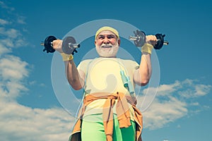 Portrait of senior man holding dumbbell. Senior man in health club. Senior man exercising on blue sky. Senior man in his