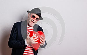 Portrait of a senior man in love in a studio, holding a red heart balloon.