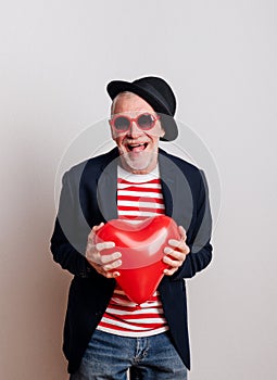 Portrait of a senior man in love in a studio, holding a red heart balloon.