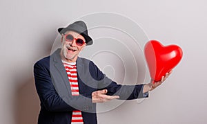 Portrait of a senior man in love in a studio, holding a red heart balloon.