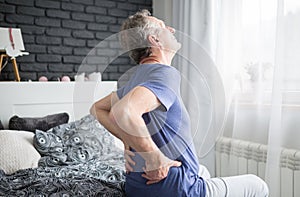 Senior man with lower back pain siting on bed photo