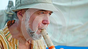 Portrait of senior man playing bamboo flute on the beach next to fishing boat