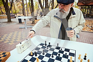 Portrait of senior man playing chess in the park on a daytime in fall. Checkmate. Concept of leisure activity, old