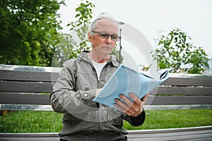 Portrait of senior man reading on bench during summer day.