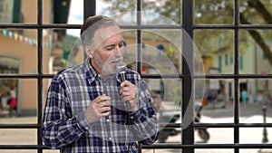 Portrait of senior man singing in the microphone standing indoors.