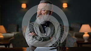 Portrait of senior man sitting at table with crossed hands in vintage cabinet.