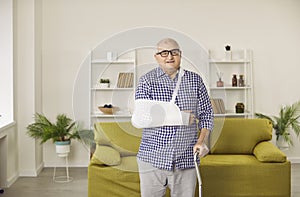 Portrait of a senior man standing in rehabilitation with crutch and with arm in a plaster cast.