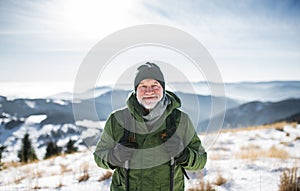 Portrét staršieho muža stojaceho v zasneženej zimnej prírode, pri pohľade na fotoaparát.