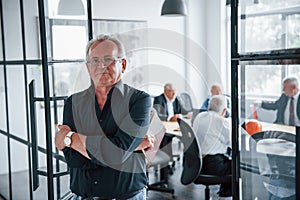 Portrait of senior man that stands in front of aged team of elderly businessman architects that have a meeting in the