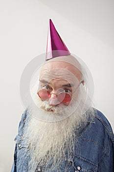 Portrait of senior man wearing red glasses and party hat against gray background