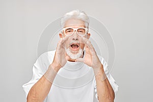 Portrait of senior man in white shouting loudly with hands, news, palms folded like megaphone