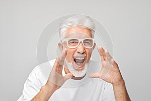 Portrait of senior man in white shouting loudly with hands, news, palms folded like megaphone