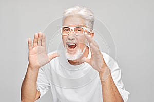 Portrait of senior man in white shouting loudly with hands, news, palms folded like megaphone