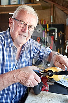 Portrait Of Senior Man Working On Model Radio Controlled Aeroplane In Shed At Home