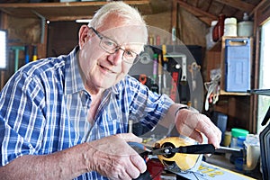 Portrait Of Senior Man Working On Model Radio Controlled Aeroplane In Shed At Home