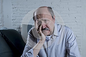 Portrait of senior mature old man on his 60s at home couch alone feeling sad and worried suffering pain and depression