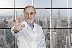 Portrait of senior medic doctor in white coat shows no reject sign by his hand.