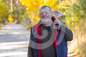 Portrait of senior musician with mandolin on the shoulder standing on a country road in an autumnal forest