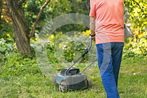 Portrait of senior old man using lawn mower in the garden on summer day