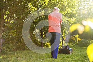 Portrait of senior old man using lawn mower in the garden on summer day