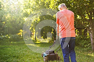 Portrait of senior old man using lawn mower in the garden on summer day