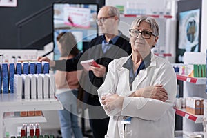 Portrait of senior pharmacist looking at camera while standing with arm crossed in pharmacy