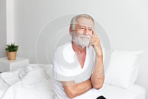 Portrait of a senior retirement man sitting and thinking alone on bed in his home