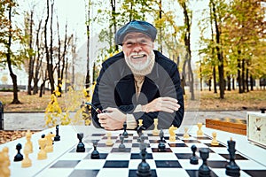 Portrait of senior smiling man playing chess in the park on a daytime in fall. Concept of leisure activity, old
