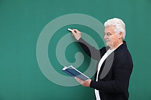 Portrait of senior teacher with book and chalk at green board