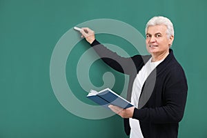 Portrait of senior teacher with book and chalk at green board