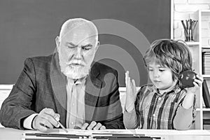 Portrait of senior teacher and little boy kid sitting at desk in classroom. Pupil and Teacher in classroom. Senior